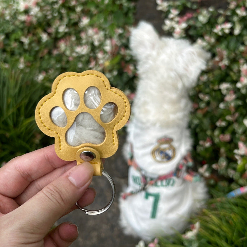 Llavero de cuero con forma de huella y ventanas transparentes con el pelo de un perro dentro, sujeto en una mano
